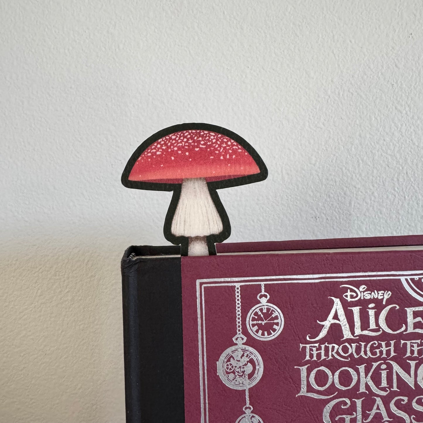 Mushroom-shaped bookmark on a book titled 'Alice Through the Looking Glass'.